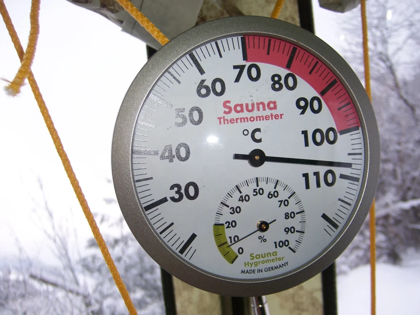 Thermometer im Saunazelt Mobiba MB-10 A2 Thermometer im Saunazelt Mobiba MB-10 A2 zeigt 108 °C und 8 % Luftfeuchtigkeit; durch das Fenster erkennt man winterliche Schneelandschaft.